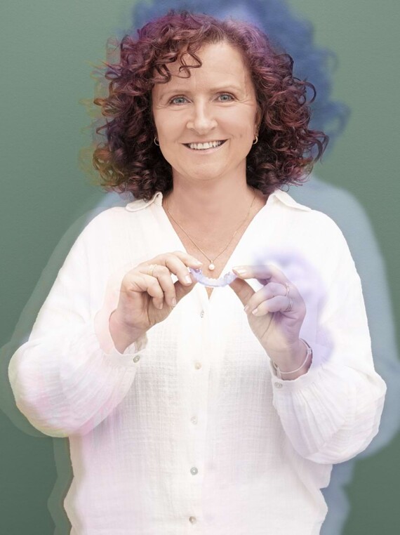 Woman in white blouse, smiling towards the camera, holding aligners in her hands